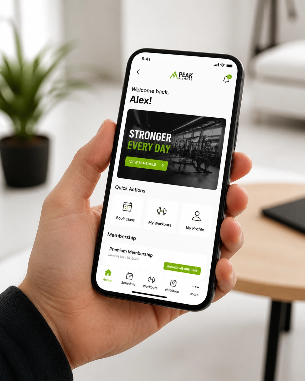 A close-up shot of a smartphone held in a hand, displaying a custom mobile application interface for a local business like a gym or contractor. The app design is modern, with white backgrounds and vibrant green buttons. The setting is a bright, airy indoor space with minimalistic decor. Clean, professional photography.