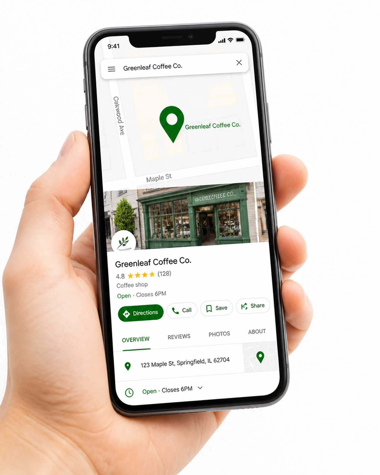 A close-up of a modern smartphone held in a hand. The screen displays a Google Maps interface with a prominent green location pin over a local business storefront.