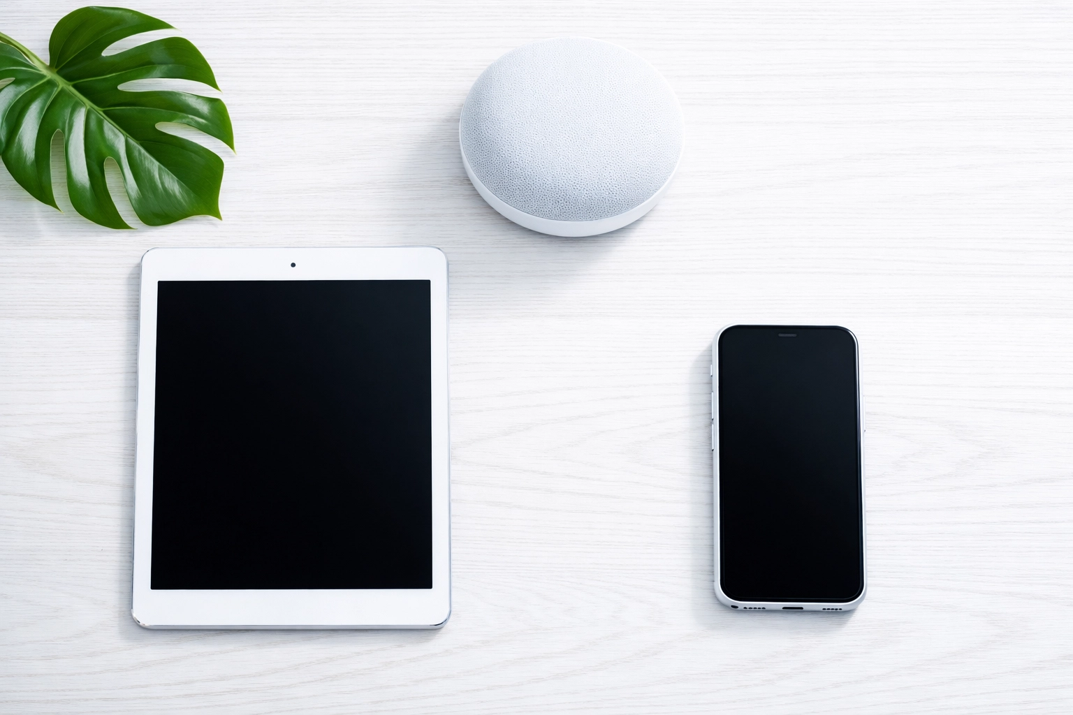 Multi-device digital ecosystem showing a tablet, smartphone, and smart speaker on a desk.
